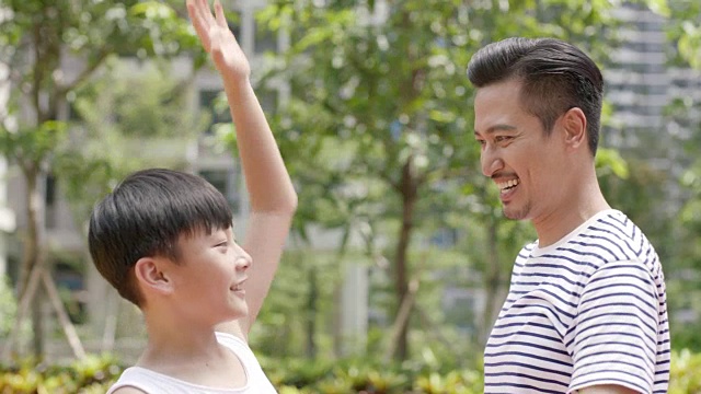 亚洲父亲和儿子欢呼得分在户外篮球运动在早上