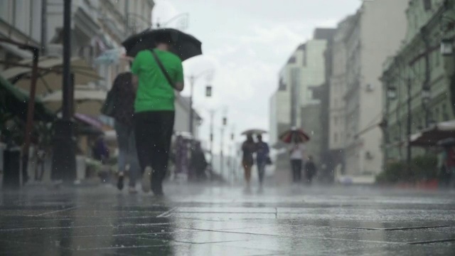 背景大雨天在城市街道。真正的时间。人们在雨中带着雨伞上下班。年轻女孩拿着五颜六色的雨伞。模糊的散景。自然背景