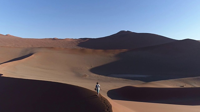 空中平移的男性游客走在納米布沙漠的一個巨大沙丘的頂部