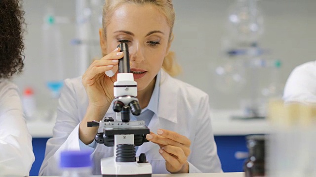 用显微镜工作的女科学家与混合种族研究小组在实验室讨论研究结果