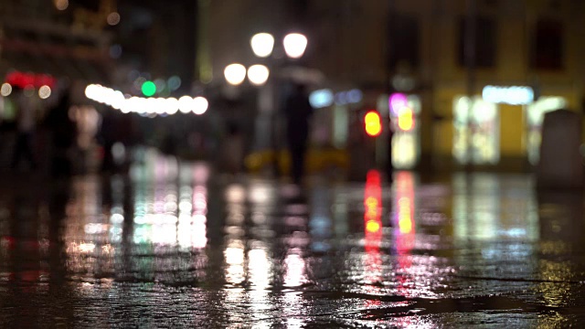 抽象明亮模糊的背景与雨滴落在多彩的沥青照明路灯和交通灯。身份不明的女孩在雨夜的城市街道上。积极的生活方式，休闲的概念，季节，天气，生活方式