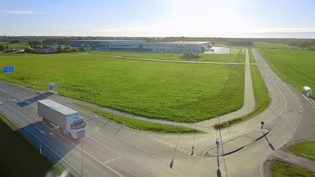 在高速公路上驾驶的白色半挂车鸟瞰图。在后台仓库和农村地区，阳光普照。