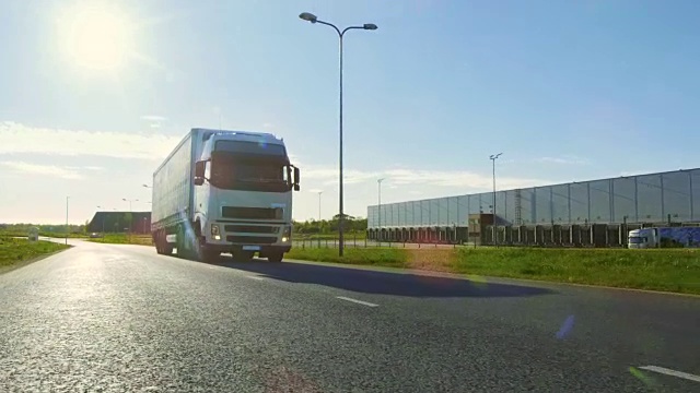 大型白色半挂车与货物拖车移动在工业仓库区域的空旷道路与阳光照耀的背景。