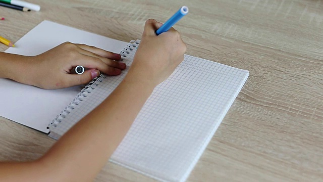 小女孩用纸笔记本给学校写信。年轻的女孩坐在桌子旁边。白人女孩写信写错了。修正毡笔的错误。家庭作业女学生写下来。