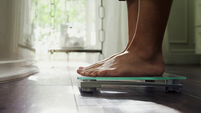 一个女人在家里用磅秤检查她的体重，4k