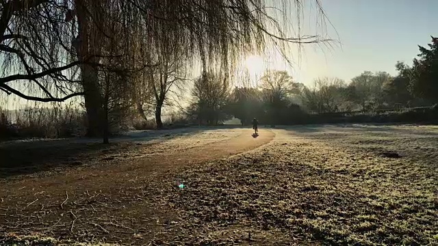 一个寒冷的早晨，一个小男孩骑着家庭自行车在湖边的一个美丽的英国小镇上骑行