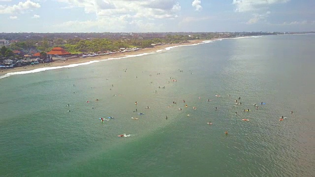 空中镜头光斑:在巴厘岛沧古的沙滩上，冲浪者挤成一排