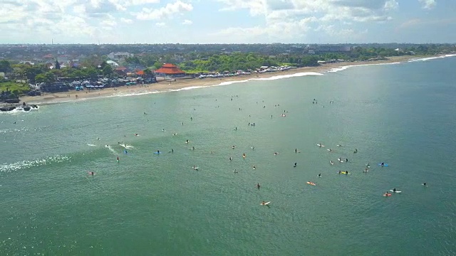 AERIAL:在阳光明媚的巴厘岛，成群的冲浪者在沧谷沙滩上排队