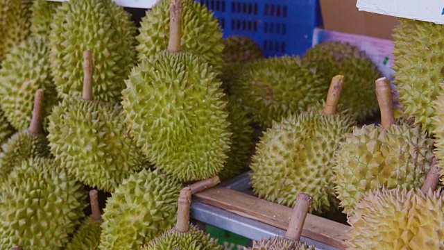 一个小贩在当地市场的街道上摘榴莲卖给顾客。榴莲是东南亚许多人心目中的水果之王。