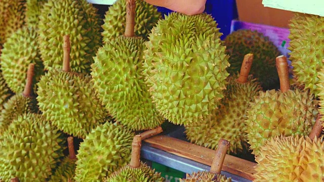 一个小贩在当地市场的街道上摘榴莲卖给顾客。榴莲是东南亚许多人心目中的水果之王。