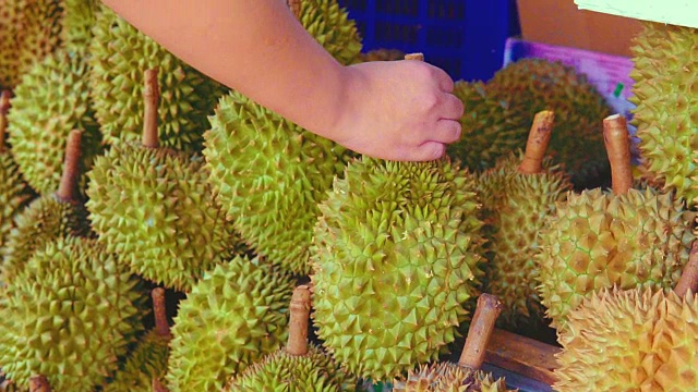 詳情圖-一個(gè)小販在當(dāng)?shù)厥袌?chǎng)的街道上摘榴蓮賣給顧客。榴蓮是東南亞許多人心目中的水果之王。