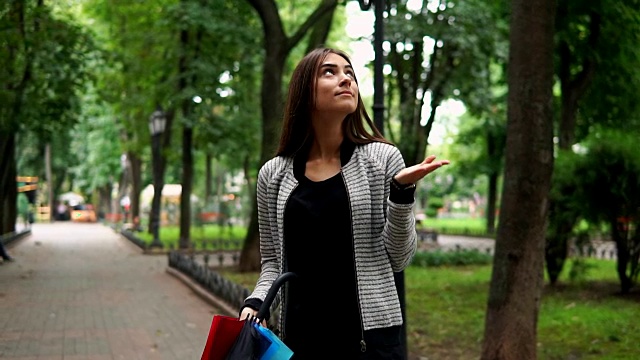 一个年轻迷人的黑发女人的肖像与她的彩色雨伞在她的手检查是否下雨在城市公园。然后她正在打开她的伞。Slowmotion拍摄