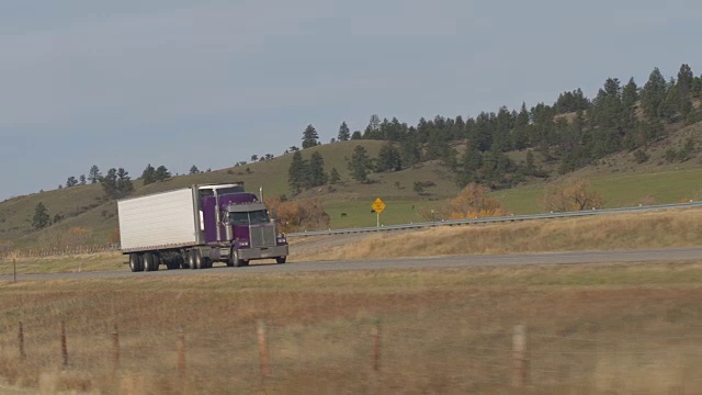 空中近距离拍摄沿着牧场的高速公路上的紫色半挂车