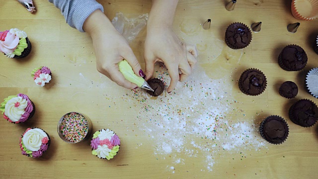 俯视图女性的手装饰巧克力纸杯蛋糕。年轻女子用糕点袋装奶油