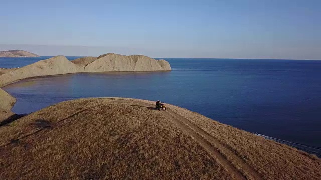 空中拍摄从飞行的无人机，一对年轻的游客正在享受美丽的海景日落慢动作，而乘坐的ATV运输。一对夫妇在海边的小山上骑着四轮自行车。4 k