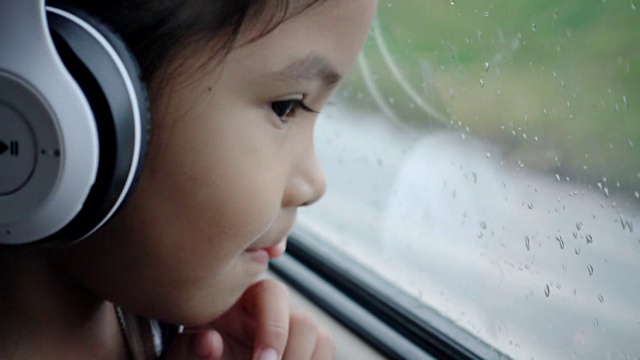 亚洲漂亮的女孩听音乐耳机移动在汽车和看在雨天