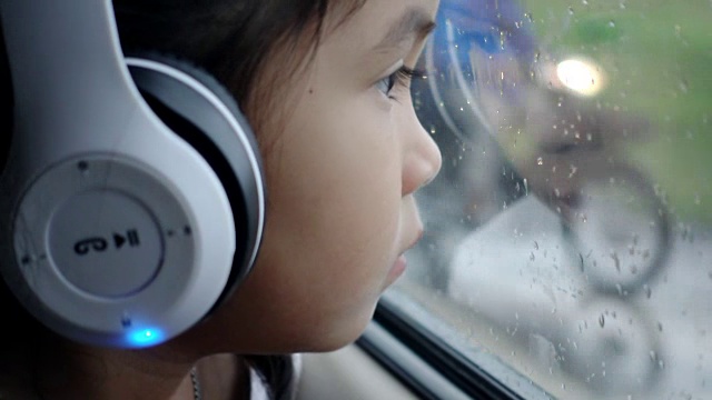 亚洲漂亮的女孩听音乐耳机移动在汽车和看在雨天