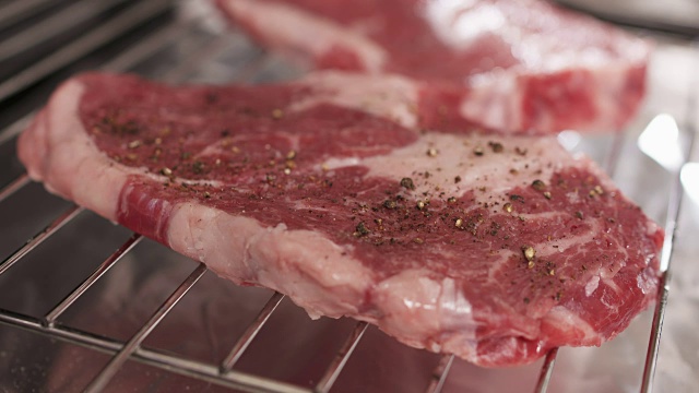 冷却架上的两块生牛肉。将新鲜牛排洒上胡椒