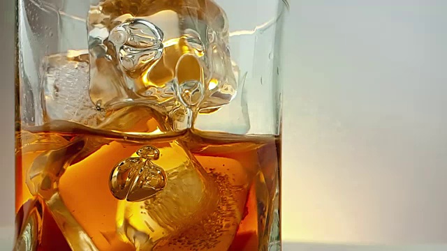 特写的酒保倒威士忌在饮用玻璃与冰块在温暖的白色背景，时间放松喝威士忌