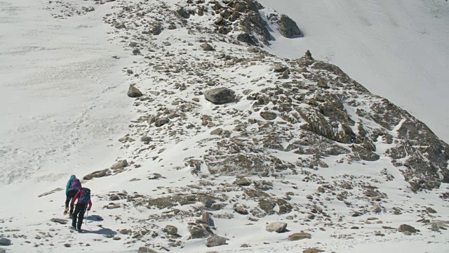 两名登山者正在岩石山脊上的冰川边缘攀登。