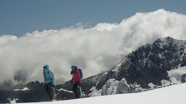 两名女登山运动员穿过高山中的冰川山脊，风暴云正在酝酿。