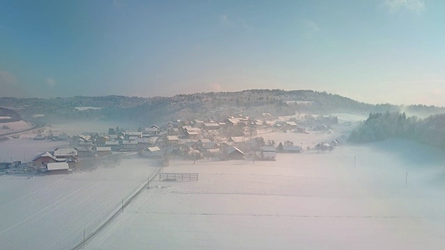 AERIAL:雾气弥漫的早晨，被白雪包围的可爱的乡村小镇