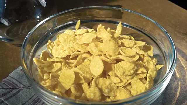 把脆黄的玉米片放进碗里，为早上一顿美味的早餐配上牛奶。慢动作旋转跟踪镜头。