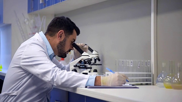 穿着实验服的经验丰富的科学家通过显微镜观察并做笔记