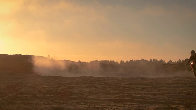 职业摩托车越野赛车手在越野沙地上骑着他的FMX摩托车。夕阳西下，薄雾笼罩大地。