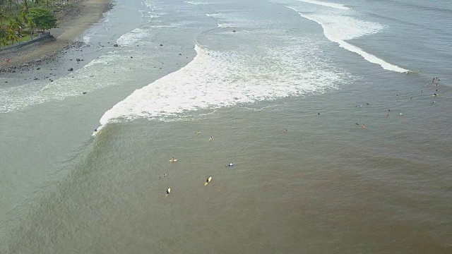 航拍:在巴厘岛冲浪点，冲浪者们在脏水上等待海浪