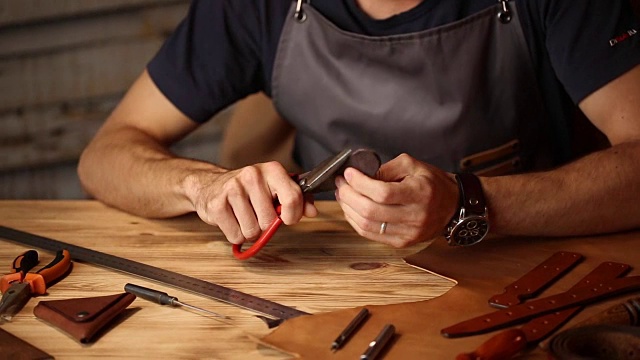 皮带在皮革车间的工作过程。手持制作工具的人正在工作。旧制革厂的皮匠。木桌上背景