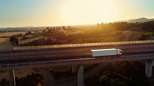 詳情圖-空中拍攝的一個白色卡車與貨物裝載移動在巨大的橋上與交通在農(nóng)村地區(qū)。背景是美麗的自然風(fēng)景。