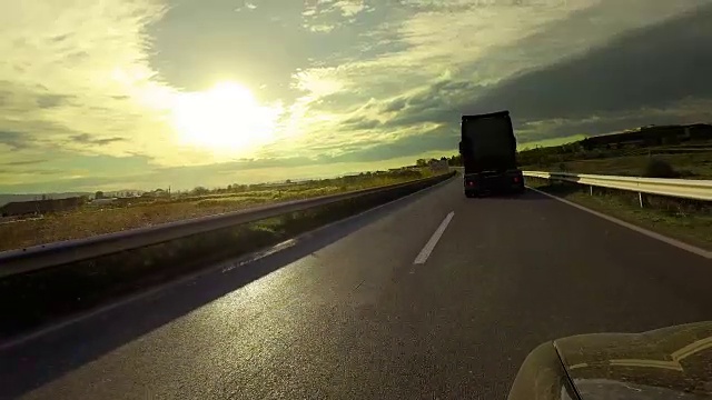 在夕阳下的乡村道路上，快速的卡车车厢超越了汽车