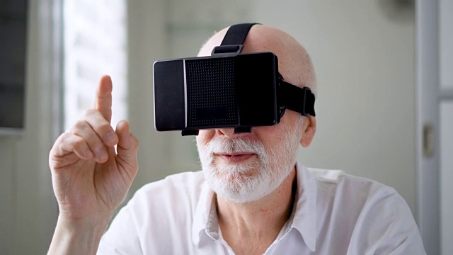 詳情圖-英俊的白色老人在家里使用VR,360眼鏡。做瀏覽，縮放和點擊手勢