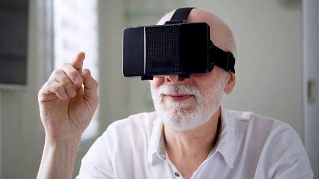 詳情圖-英俊的白色老人在家里使用VR,360眼鏡。做瀏覽，縮放和點擊手勢