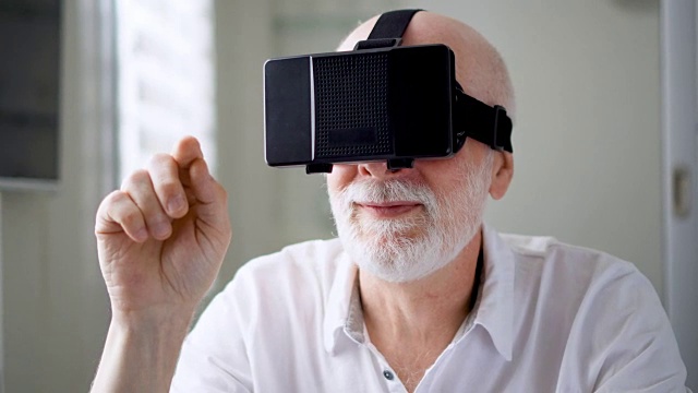 詳情圖-英俊的白色老人在家里使用VR,360眼鏡。做瀏覽，縮放和點擊手勢