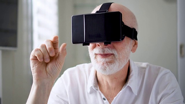 詳情圖-英俊的白色老人在家里使用VR,360眼鏡。做瀏覽，縮放和點擊手勢