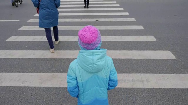 年轻女孩通过人行横道过马路。穿蓝色夹克的女孩放学回家。