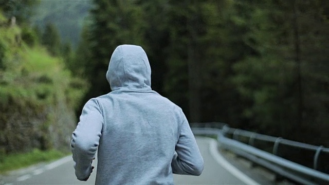 男子在山路上慢跑，无脸背近看慢动作。清晨独自跑在户外，穿着灰色连帽毛衣。跑步运动员在大自然中进行短跑、锻炼和训练。自由和选择