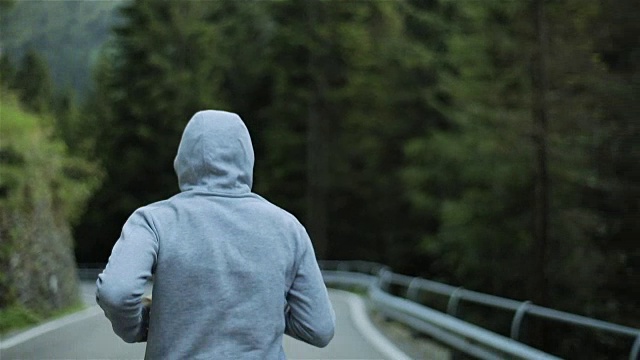 详情图-男子在山路上慢跑,无脸背近看慢动作。清晨独自跑在户外,穿着灰色连帽毛衣。跑步运动员在大自然中进行短跑、锻炼和训练。自由和选择