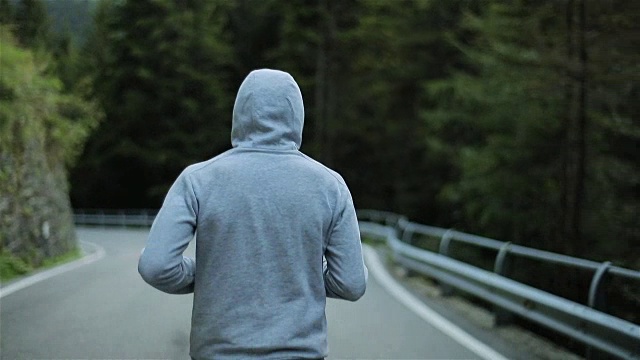 详情图-男子在山路上慢跑,无脸背近看慢动作。清晨独自跑在户外,穿着灰色连帽毛衣。跑步运动员在大自然中进行短跑、锻炼和训练。自由和选择