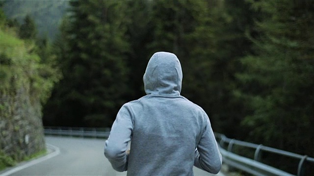 详情图-男子在山路上慢跑,无脸背近看慢动作。清晨独自跑在户外,穿着灰色连帽毛衣。跑步运动员在大自然中进行短跑、锻炼和训练。自由和选择