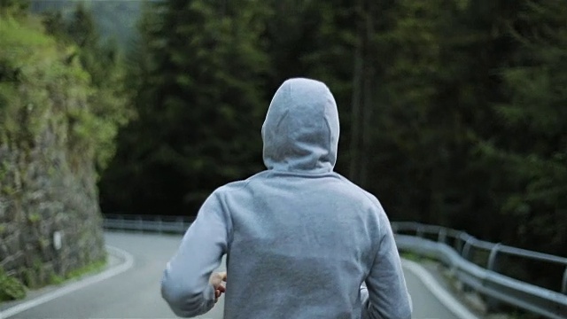 详情图-男子在山路上慢跑,无脸背近看慢动作。清晨独自跑在户外,穿着灰色连帽毛衣。跑步运动员在大自然中进行短跑、锻炼和训练。自由和选择