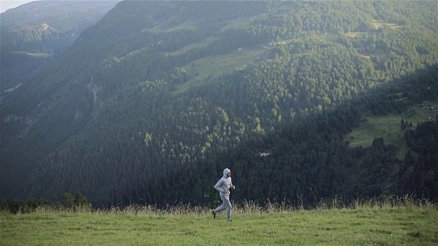 男人在户外山上慢跑，慢动作。在阳光明媚的早晨，穿着灰色运动服在小山上的草地上热身训练。运动运动健康生活方式马拉松健康理念