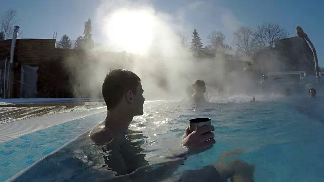 英俊的男性喝着茶放松在温泉水。冬天