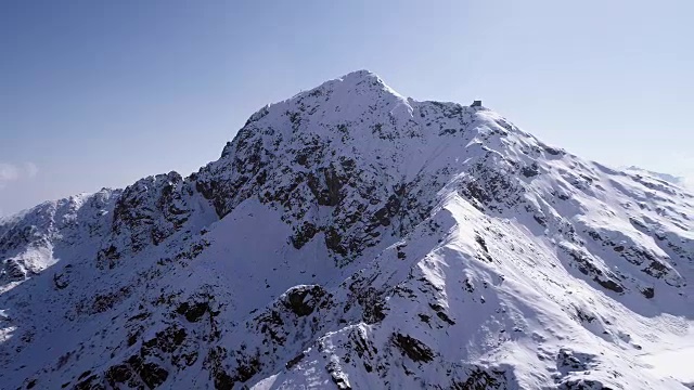 空中飞行向后移动，越过雪峰山脊建立。冬季户外雪高山野自然景观。4k无人机飞行建立镜头