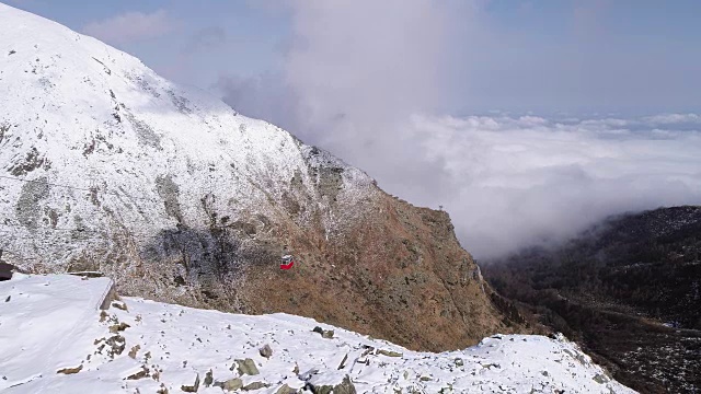 空中飞过白雪皑皑的山脊峡谷，红彤彤的缆车升起架设者。冬季户外雪高寒野生自然旅游缆车交通。4k无人机飞行建立镜头