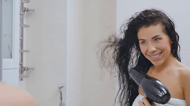 美丽的黑发女郎在镜子前慢动作地干她的头发