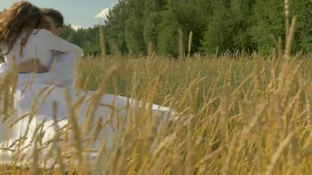 詳情圖-一名年輕女子和一名身穿白色西裝的男子逃跑，彼此相遇并擁抱。在一個陽光明媚的日子里，在一片麥田里。