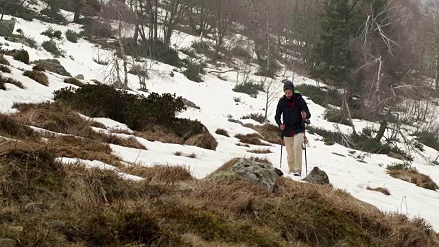 背包男徒步行走在雪道上。后一面。真正的背包客成人徒步旅行或徒步旅行在秋冬野外野外的山区自然，大雾天气恶劣。4 k的视频